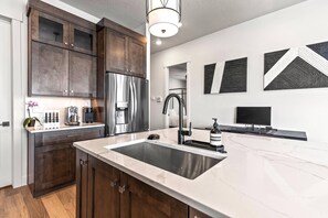 Une cuisine moderne avec des meubles de rangement en bois foncé, un réfrigérateur en acier inoxydable, un plan de travail en marbre et un évier encastré.
