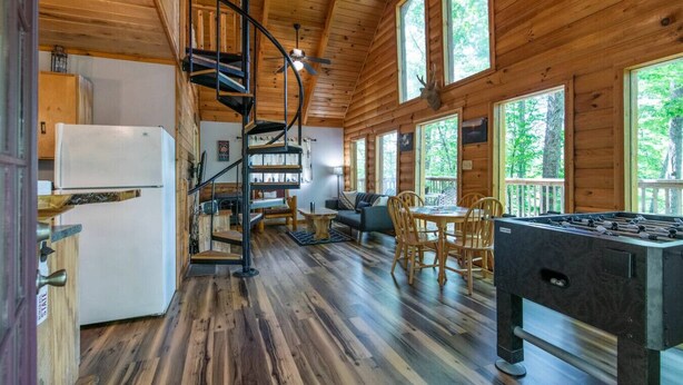 A wooden cabin interior with a spiral staircase, a dining area, and a foosball table. - Gorgeous View Cabin - in Red River Gorge, KY (Slade)