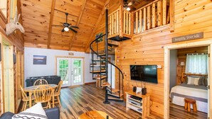 A cozy wooden cabin with a spiral staircase, a dining area, and a bedroom with a bed and TV. - Gorgeous View Cabin - in Red River Gorge, KY (Slade)