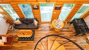 A cozy cabin interior with a wooden floor, a sofa, a dining table with chairs, a foosball table, and a spiral staircase. - Gorgeous View Cabin - in Red River Gorge, KY (Slade)