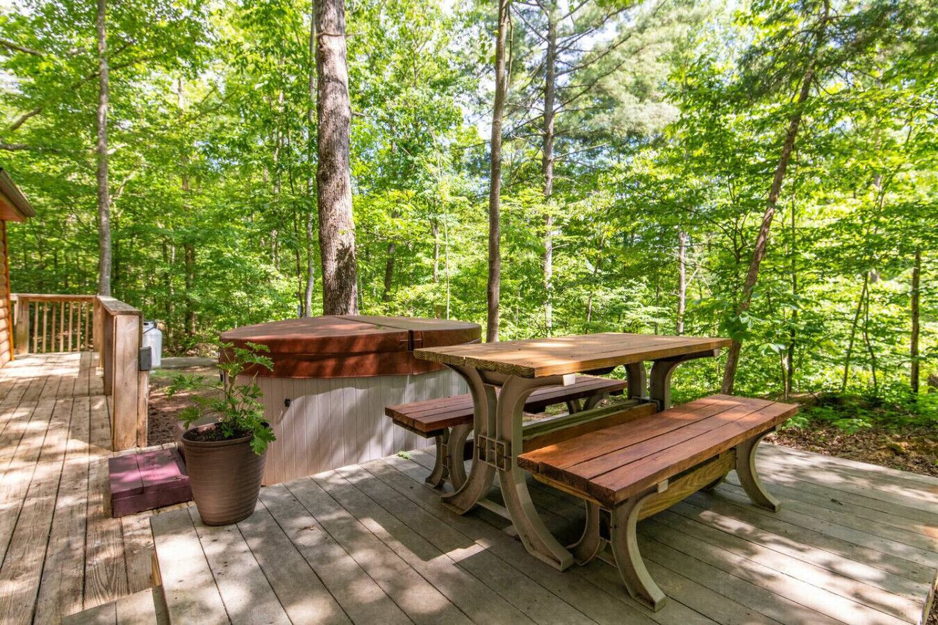 Um deck de madeira com mesa de piquenique e bancos, rodeado por uma floresta.
