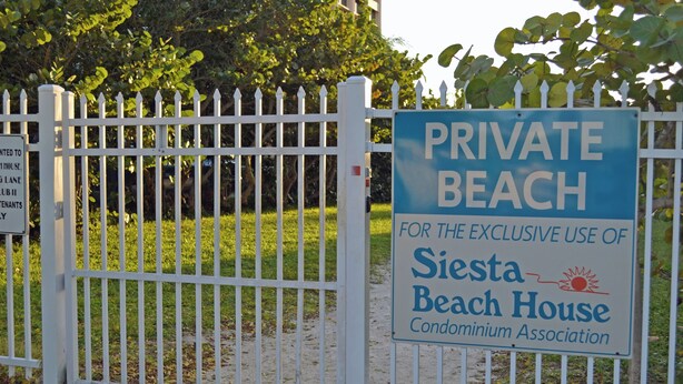 Een omheind gebied met een bord waarop staat dat het een privéstrand is, uitsluitend voor gebruik door de Siesta Beach House Condominium Association.