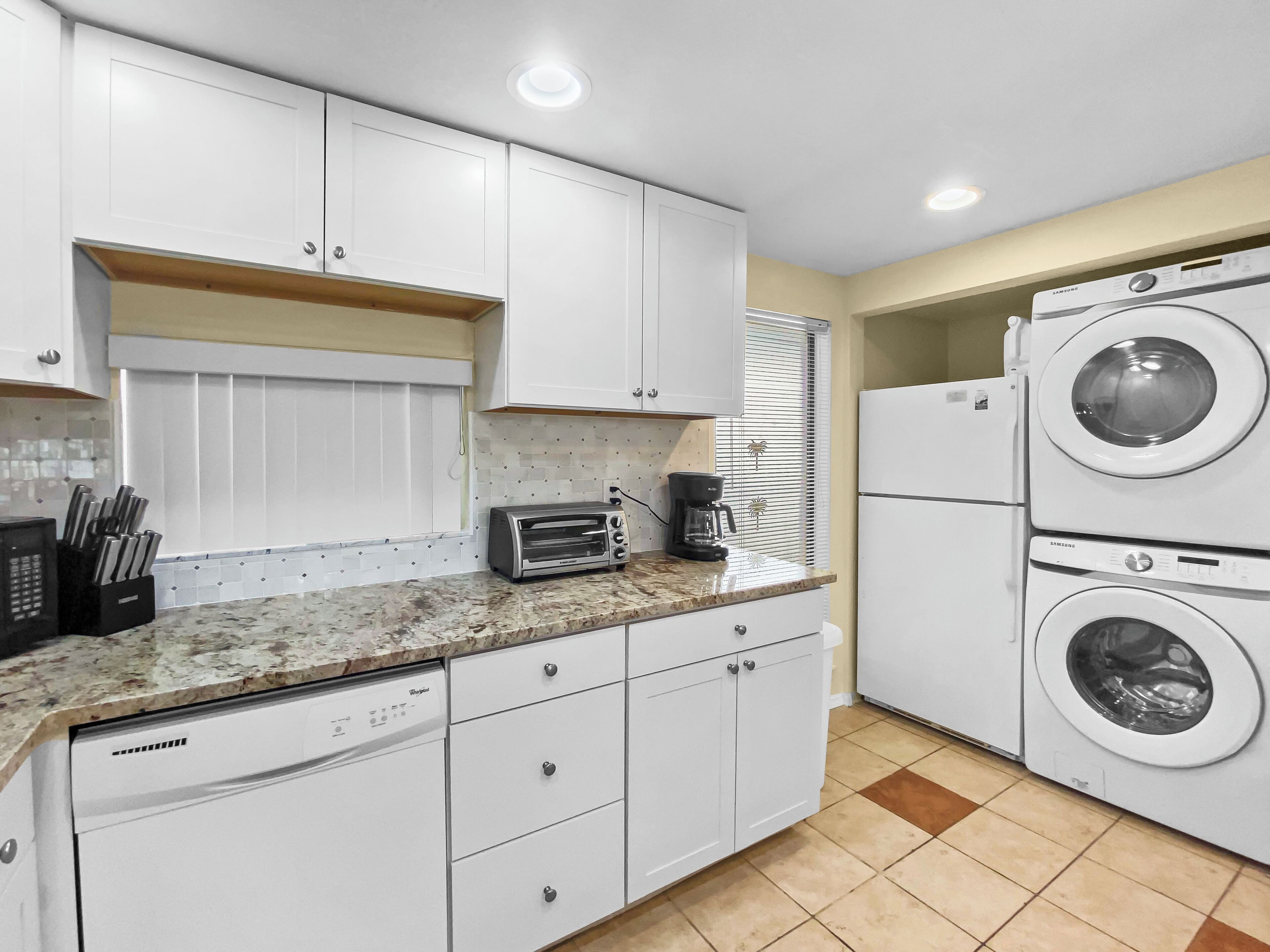 Une cuisine compacte avec des meubles blancs, un lave-vaisselle encastré, un grille-pain et un lave-linge et un sèche-linge superposés.