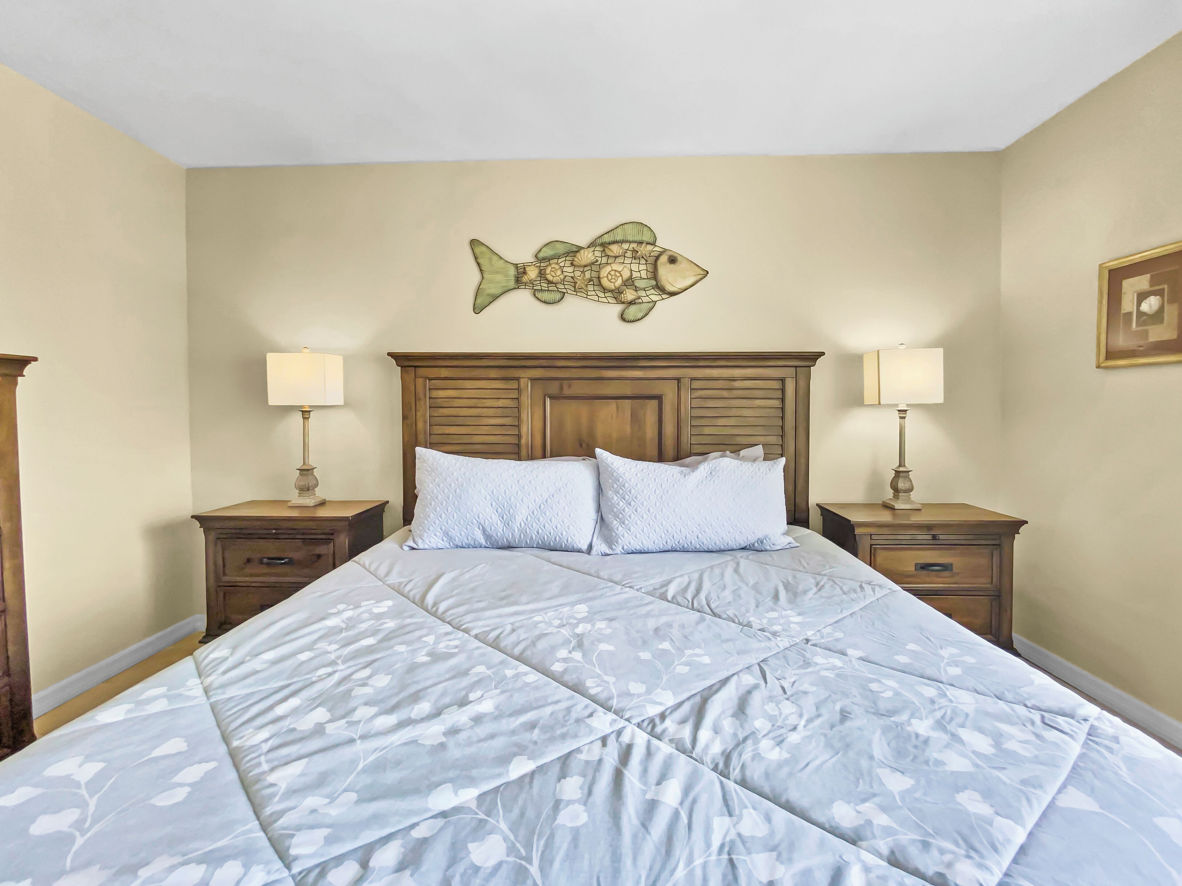 Une chambre à coucher avec un grand lit, deux tables de chevet, une tête de lit en bois et une décoration murale représentant des poissons.