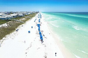 A beach with rows of blue umbrellas, white sandy beach, and buildings in the background. - Little Dipper (Santa Rosa Beach)