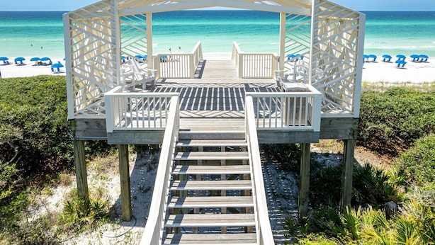 A wooden beach gazebo with a wooden deck leading to it, surrounded by beach chairs and umbrellas. - Little Dipper (Santa Rosa Beach)