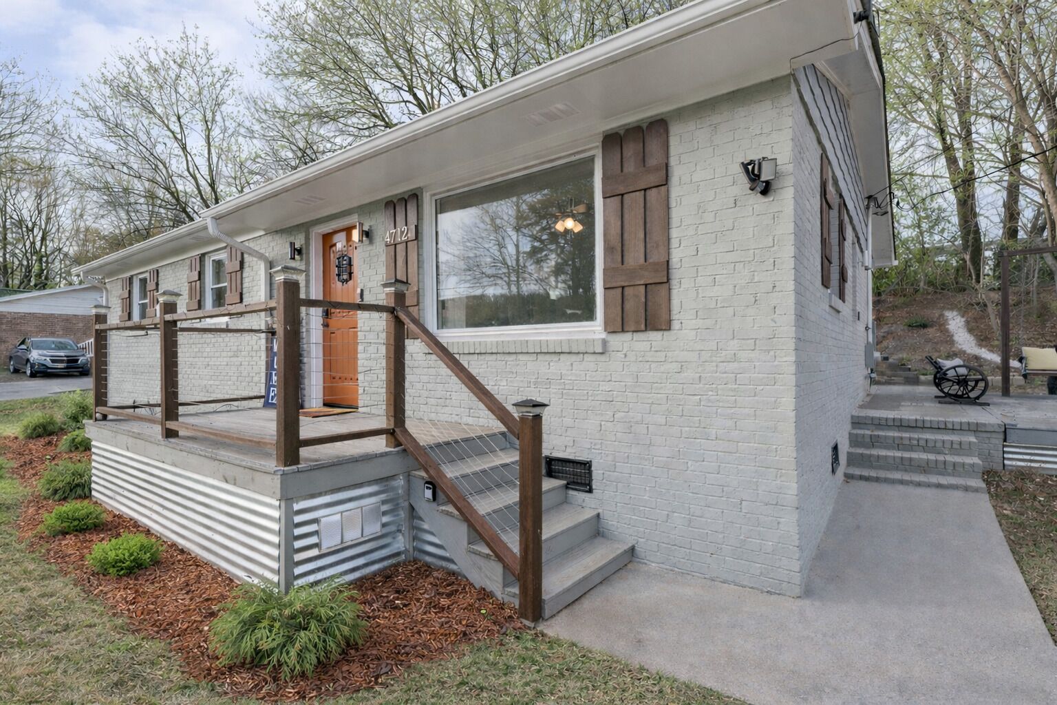 Une maison moderne de plain-pied, avec une façade en briques, une porte d’entrée en bois et un petit porche doté d’une rambarde en métal.