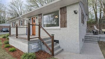 Une maison moderne de plain-pied, avec une façade en briques, une porte d’entrée en bois et un petit porche doté d’une rambarde en métal.