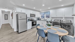 A modern kitchen with white cabinets, stainless steel appliances, and a dining area with a wooden table and blue chairs.