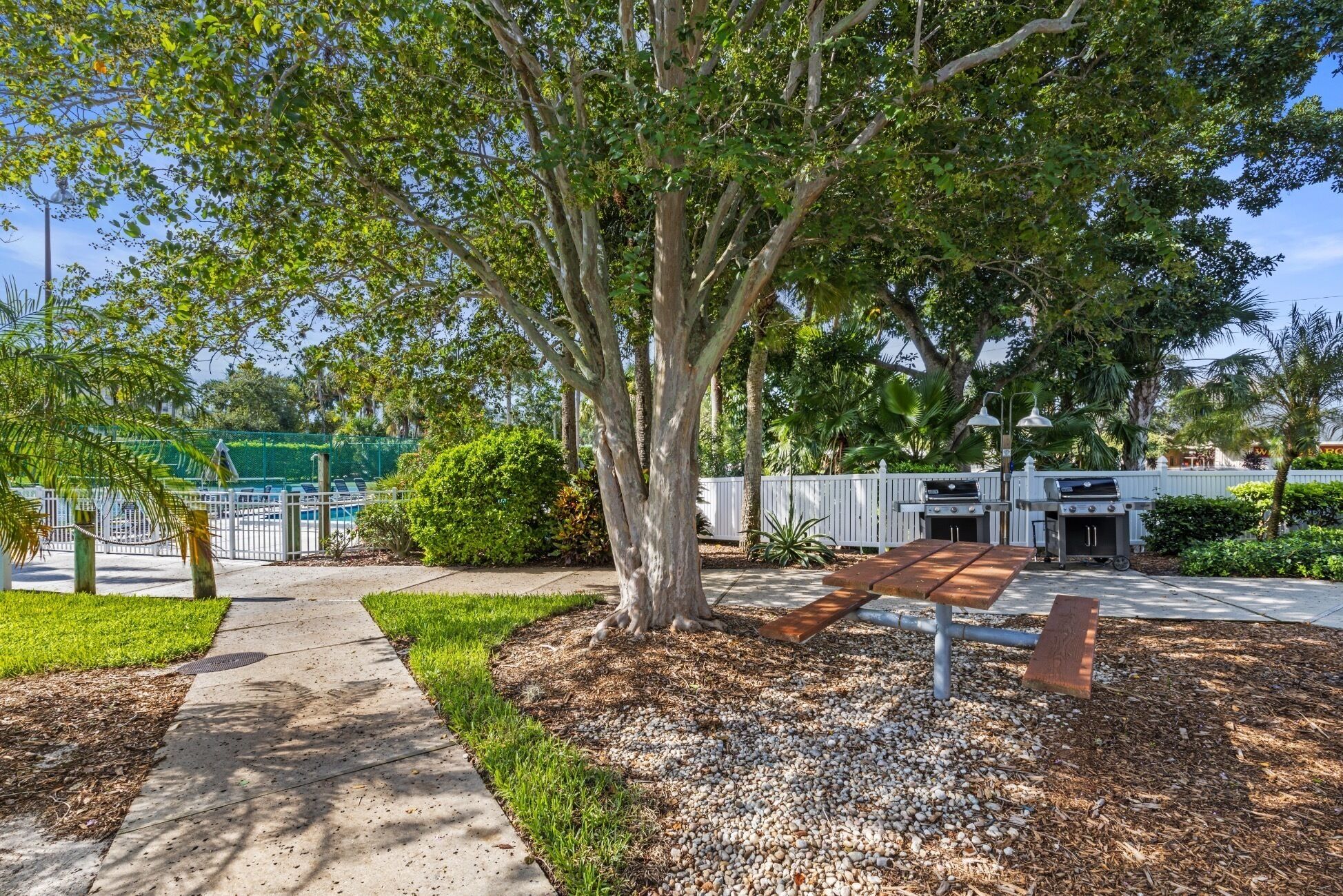 A park area with a paved walkway, a picnic table, and barbecue grills.