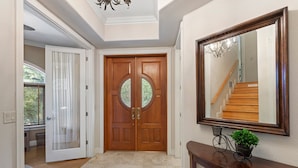 A hallway with a wooden double door, a mirror, and a potted plant on a console table. - Miramar (Siesta Key)