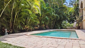 A swimming pool surrounded by lush tropical vegetation, with a paved patio area and a chair. - Miramar (Siesta Key)