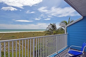 Ein Balkon mit Blick auf den Strand, einer Palme und einem blauen Stuhl.