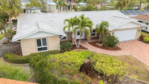A residential house with a tiled roof, a garage, and a well-maintained garden with various shrubs and a palm tree. - Waterside Villa (Siesta Key)