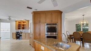 A modern kitchen with granite countertops, stainless steel appliances, wooden cabinets, and a dining area with a chandelier. - Waterside Villa (Siesta Key)