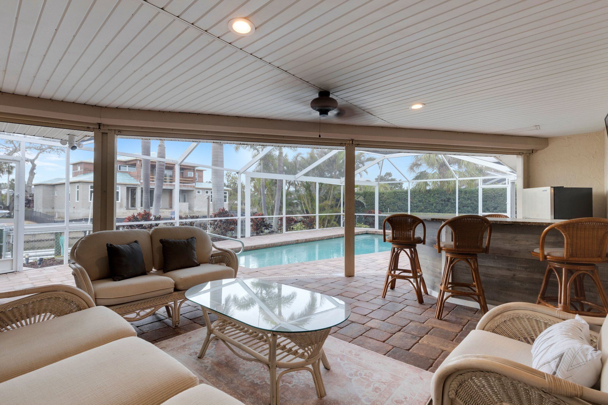 A covered outdoor area with a pool, wicker furniture, and a ceiling fan.
