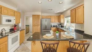 A modern kitchen with wooden cabinets, stainless steel appliances, and a central island with chairs. - Michigan Sun Lakes (Chandler)