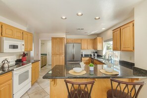 A modern kitchen with wooden cabinets, stainless steel appliances, and a central island with chairs. - Michigan Sun Lakes (Chandler)