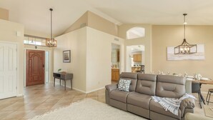 A spacious living room with a brown leather sofa, a white rug, and a dining area with a wooden table and chairs. - Michigan Sun Lakes (Chandler)