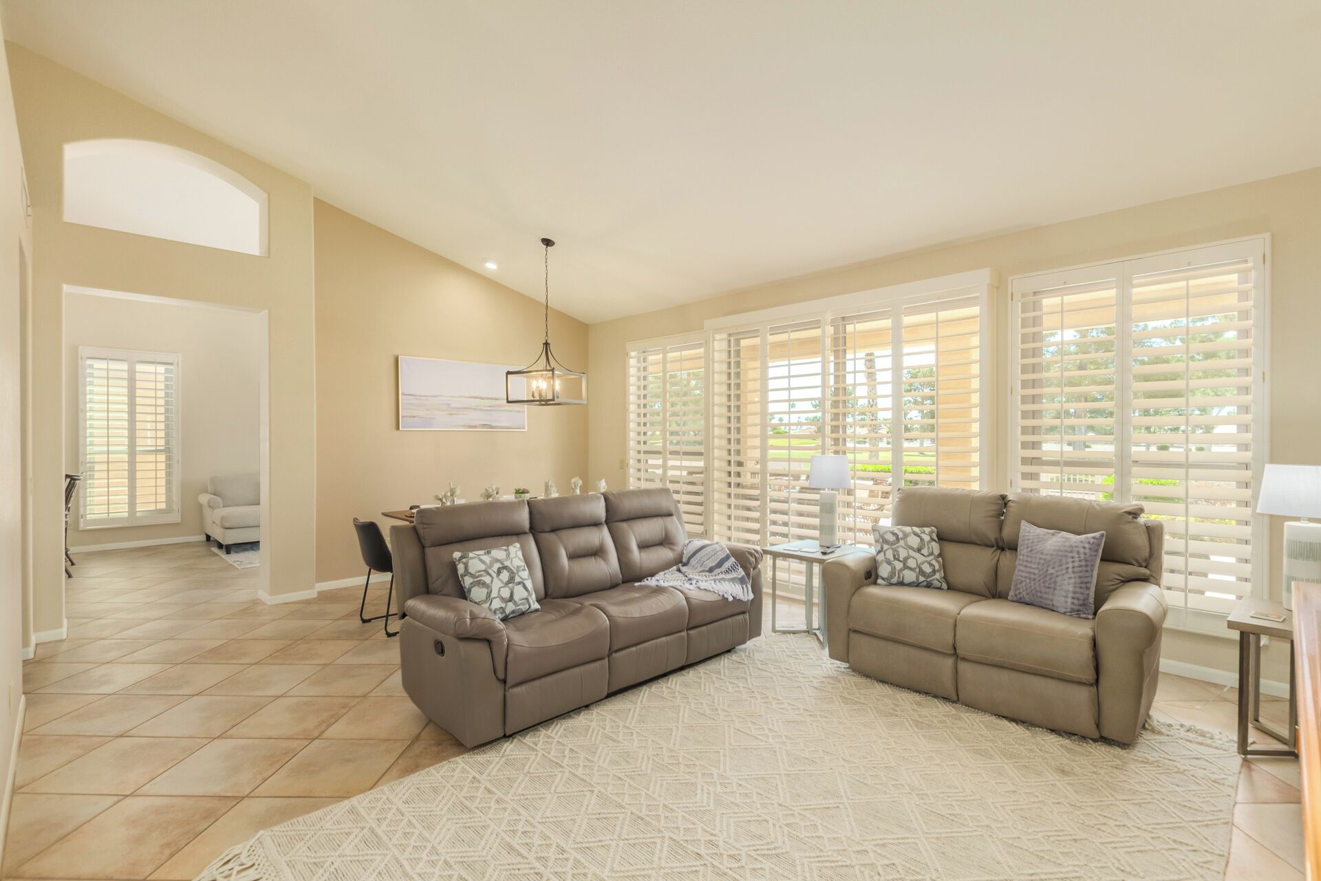 A spacious living room with two sofas, a dining area, and large windows with blinds.