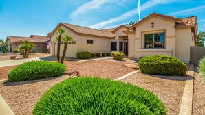 A single-story house with a tiled roof, a front porch, and a well-maintained garden with hedges and a palm tree. - Michigan Sun Lakes (Chandler)