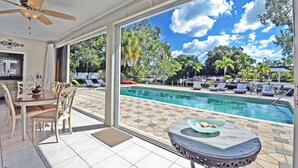 A spacious room with a large window overlooking a swimming pool, a dining area with a table and chairs, and a ceiling fan. - Edgemere (Siesta Key)