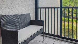 A balcony with a wicker sofa and a view of greenery. - Midnight Cove II - Sunrise (Siesta Key)
