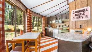 A modern kitchen with wooden cabinets, a dining area with striped flooring, and a sign reading "CAROUSEL HOUSE SUNRIVER". - Carousel House (Bend)