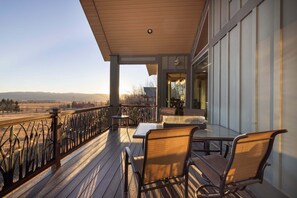 Una terraza de madera con mobiliario exterior, una mesa de vidrio y vistas al paisaje.