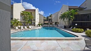 A swimming pool with lounge chairs and palm trees, surrounded by buildings with a stone-tiled patio. - Bay Oaks - E82 (Siesta Key)