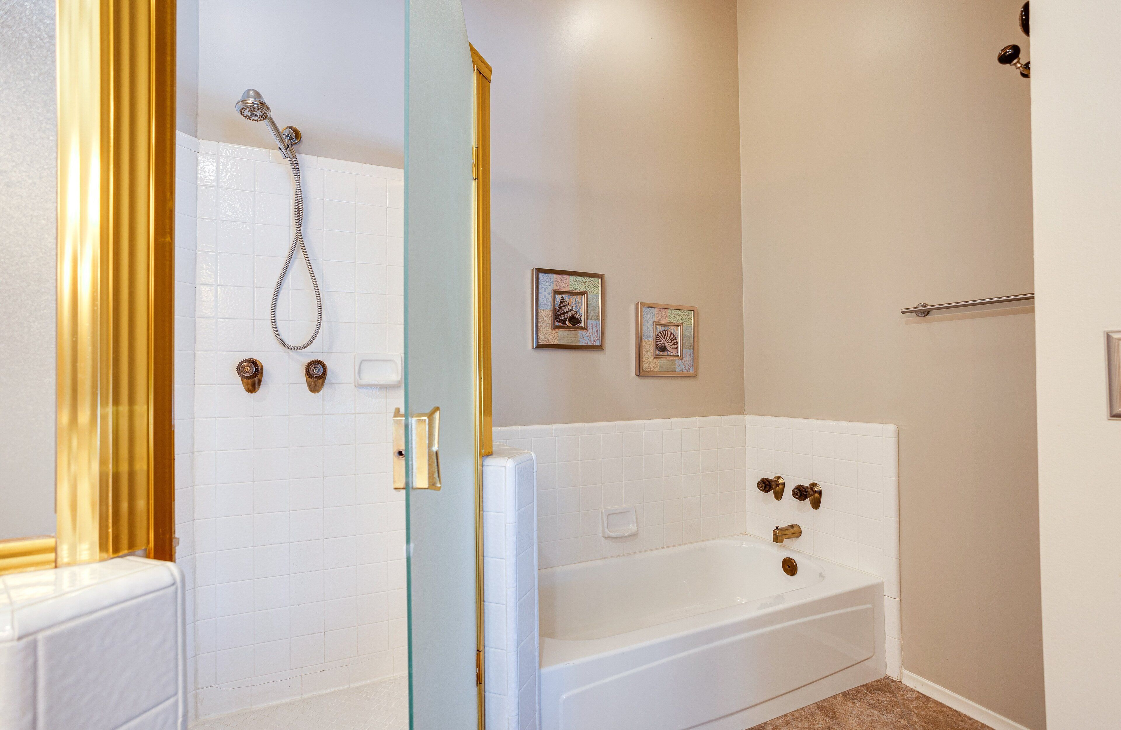 A bathroom with a shower, a bathtub, and two framed pictures on the wall.