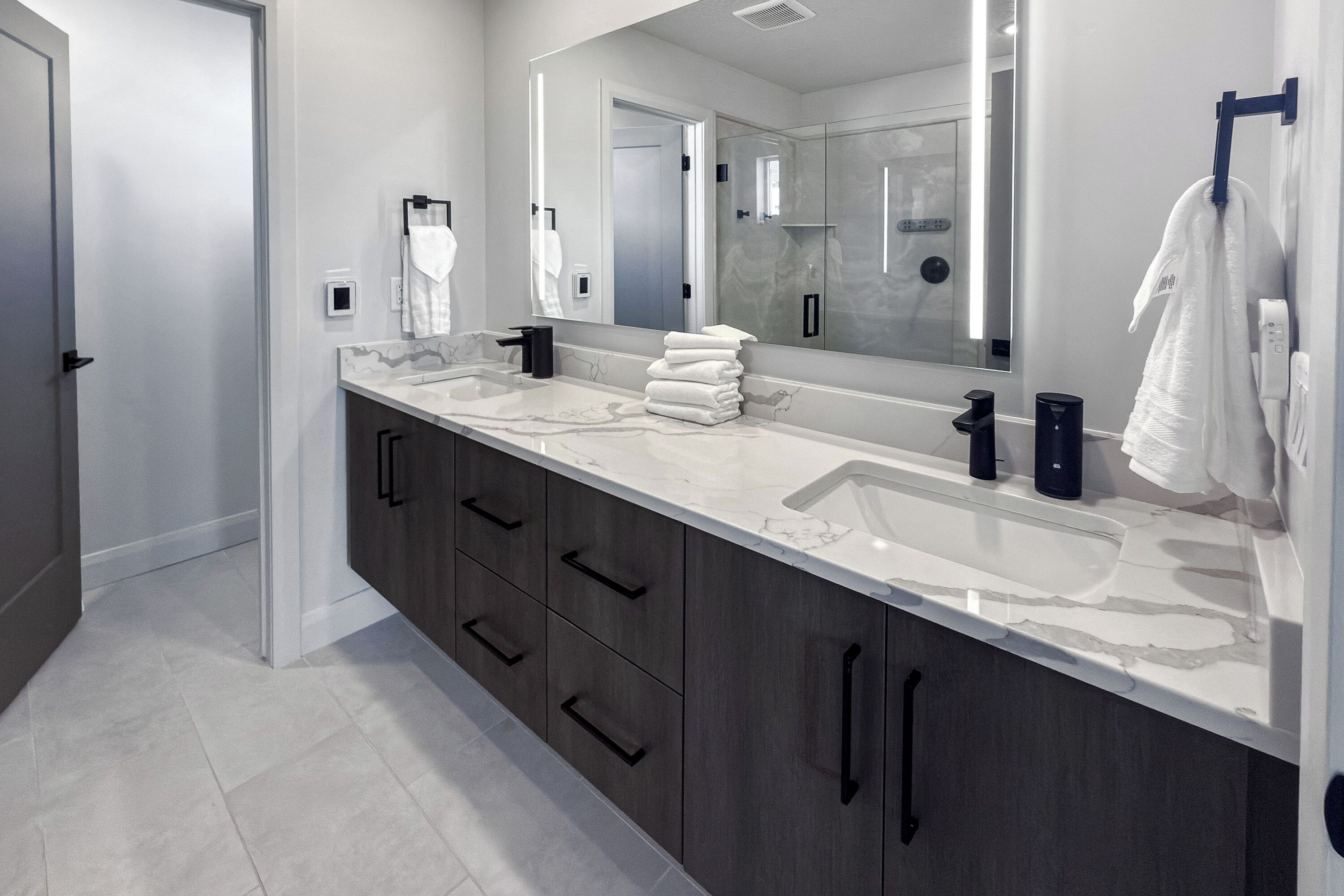 A modern bathroom with two sinks, a large mirror, and dark wooden cabinets.