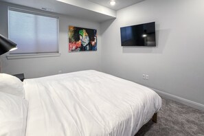 A bedroom with a large bed, a flat-screen TV mounted on the wall, and a window with blinds. - Luxury Escape - Silver Creek (Park City)