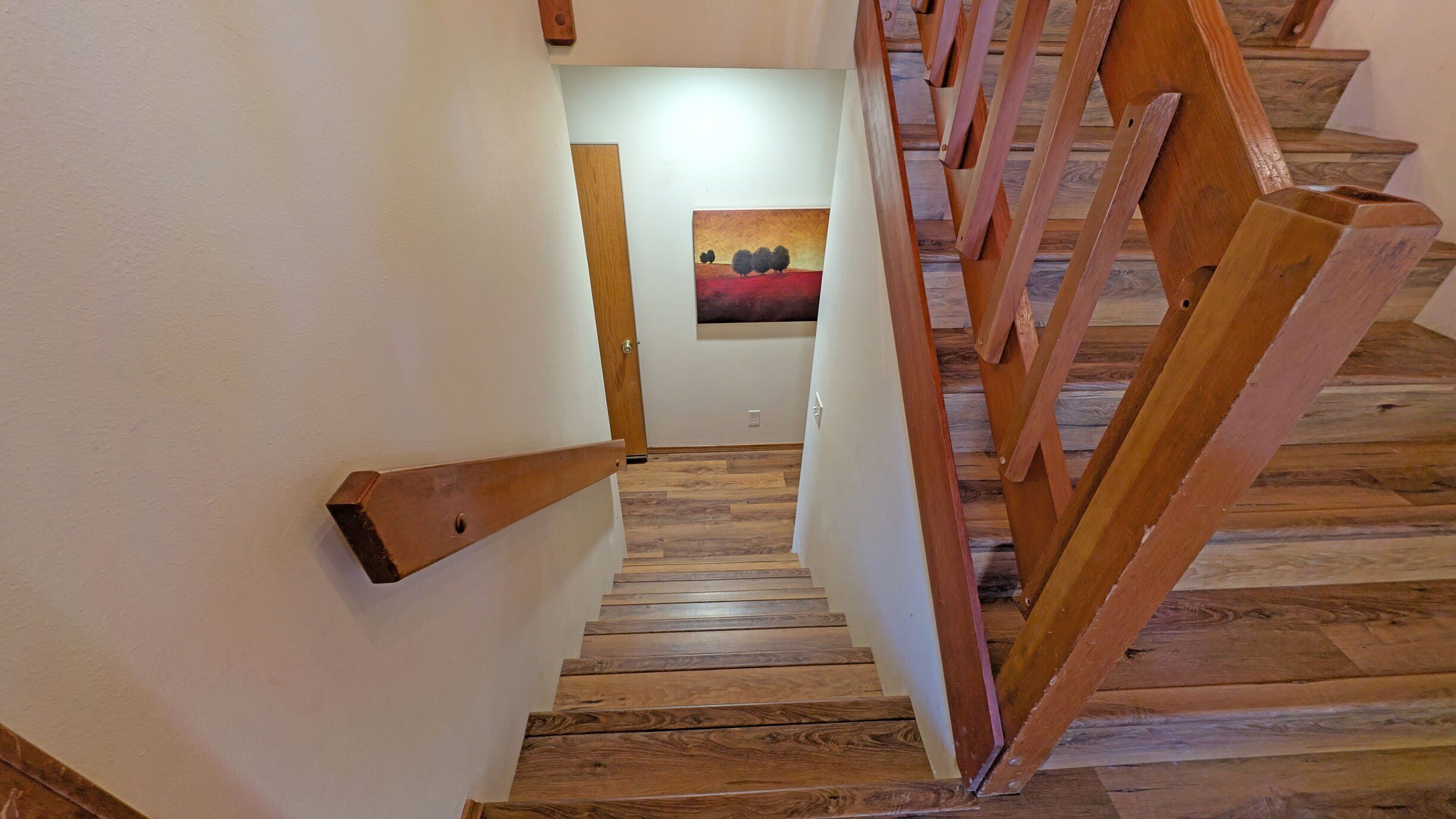 A wooden staircase with a handrail leading to a room with a painting on the wall.