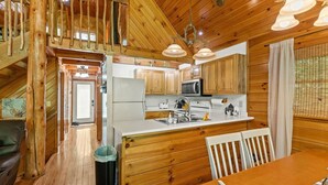 A wooden cabin interior with a kitchen, dining area, and a staircase. - Hot Tub & Wifi - Birdsong - Red River Gorge, KY (Stanton)