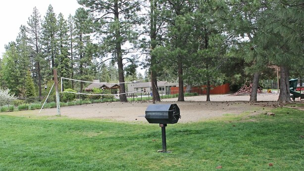 Un jardin avec un barbecue, un filet de volley-ball et une terrasse en bois.