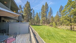 Un bâtiment moderne doté d’une terrasse, d’un espace salon extérieur et d’une pelouse bien entretenue, le tout entouré de grands arbres.