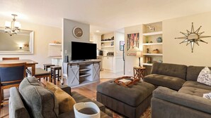 Un salon moderne avec un canapé, un pouf et un téléviseur à écran plat.
