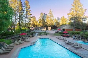 A swimming pool with lounge chairs and umbrellas, surrounded by trees and buildings.