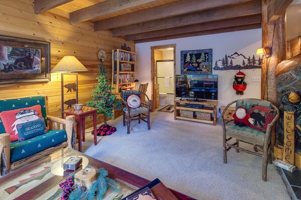 A cozy cabin interior with a wooden ceiling, a Christmas tree, a sofa, a chair, a bookshelf, and a fireplace. - Diamond Peak 2 (Bend)