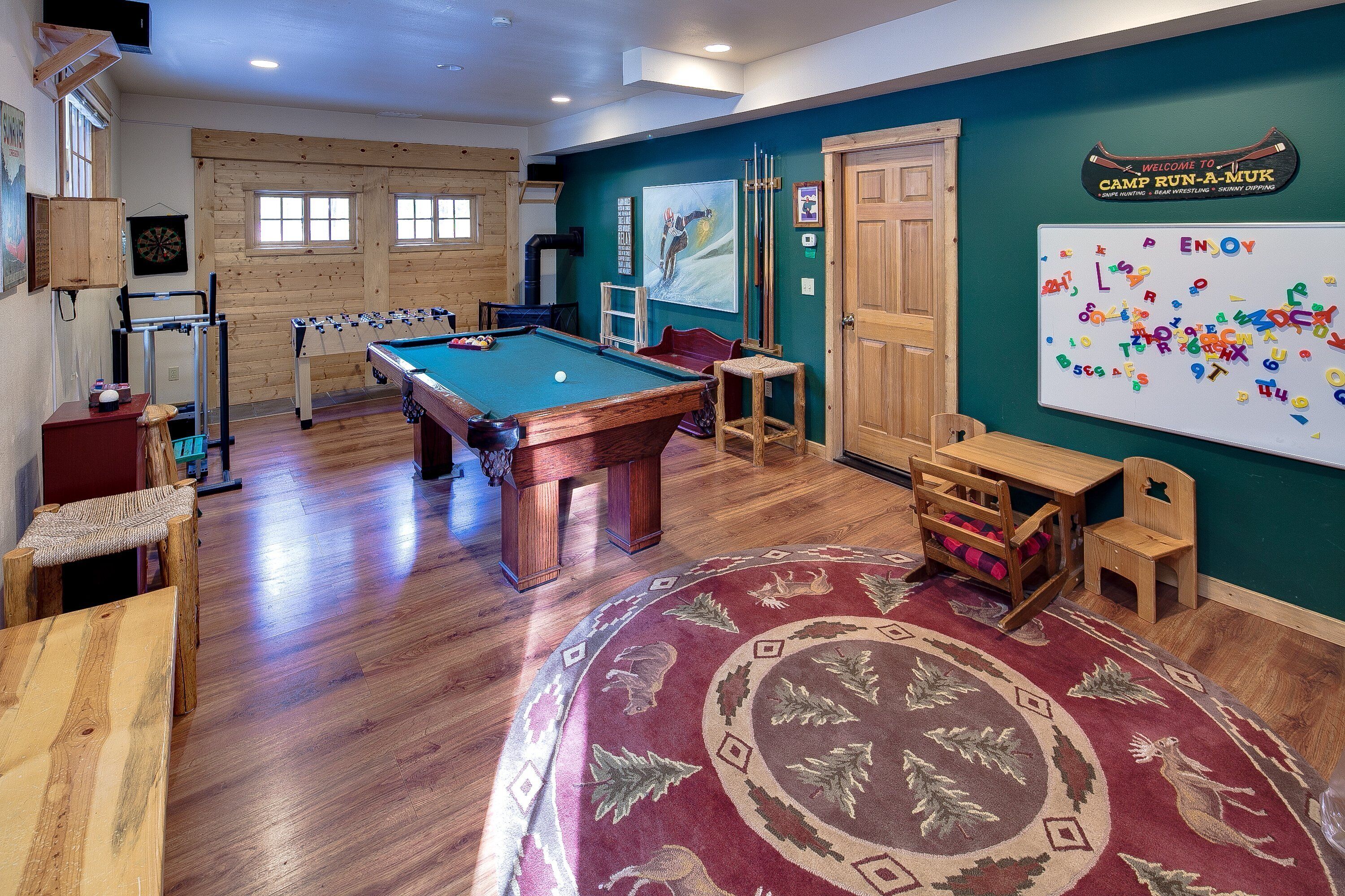A recreational room with a pool table, foosball table, dartboard, and a whiteboard with colorful letters.