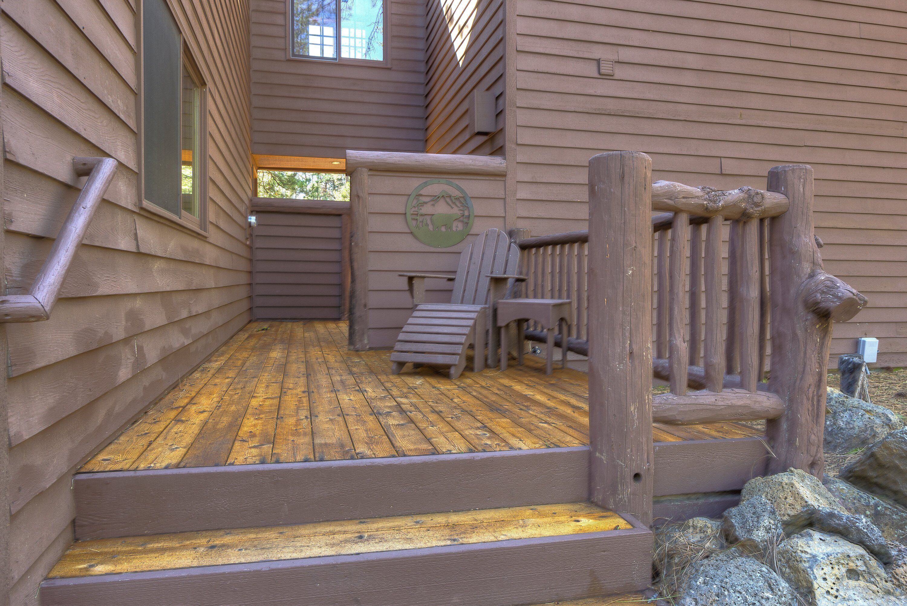 A wooden deck with steps leading to a door, a wooden chair, and a wooden railing.