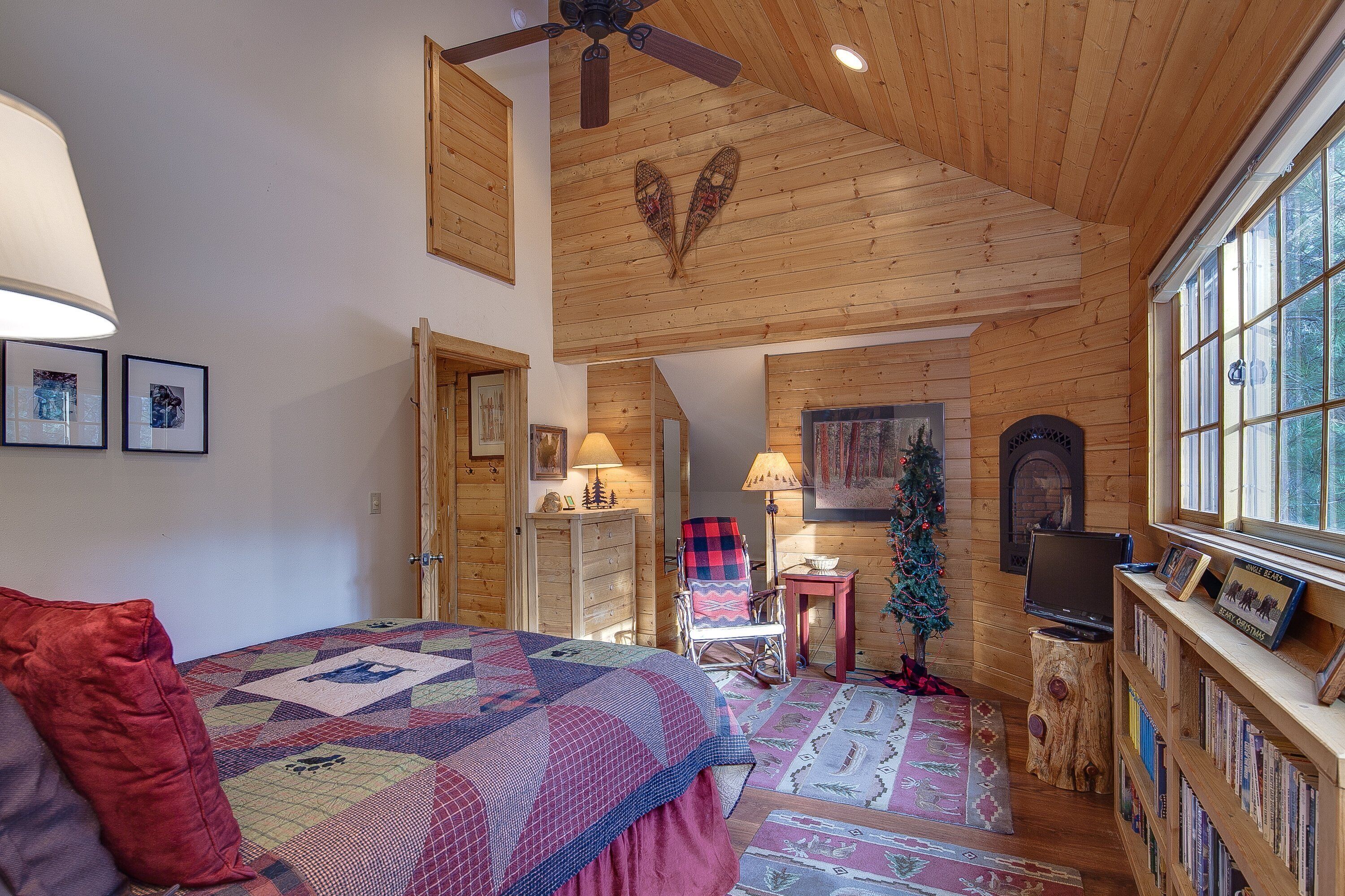 A cozy bedroom with a bed, a rocking chair, a fireplace, and a bookshelf.