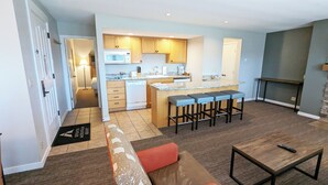 A modern kitchen with wooden cabinets, a microwave, and a coffee maker. There is a bar area with stools and a small table. - 7th Mtn 1535f (Bend)