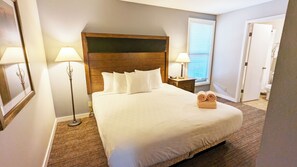 A neatly made bed with white linens and pillows, a wooden headboard, two bedside lamps, and a rolled towel on the bed. - 7th Mtn 1535f (Bend)
