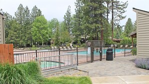 A pool area with a fenced pool, lounge chairs, and a wooden fence. - 7th Mtn 1235a (Bend)