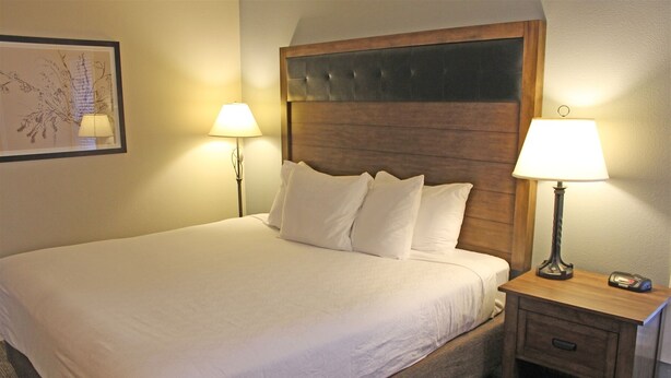 A neatly made bed with white linens, two bedside lamps, and a wooden headboard. - 7th Mtn 1235a (Bend)