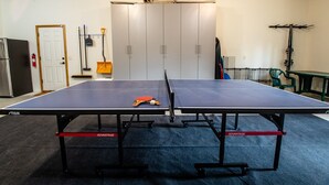 Une table de ping-pong dans une pièce qui contient une porte, des armoires et un porte-vélo.