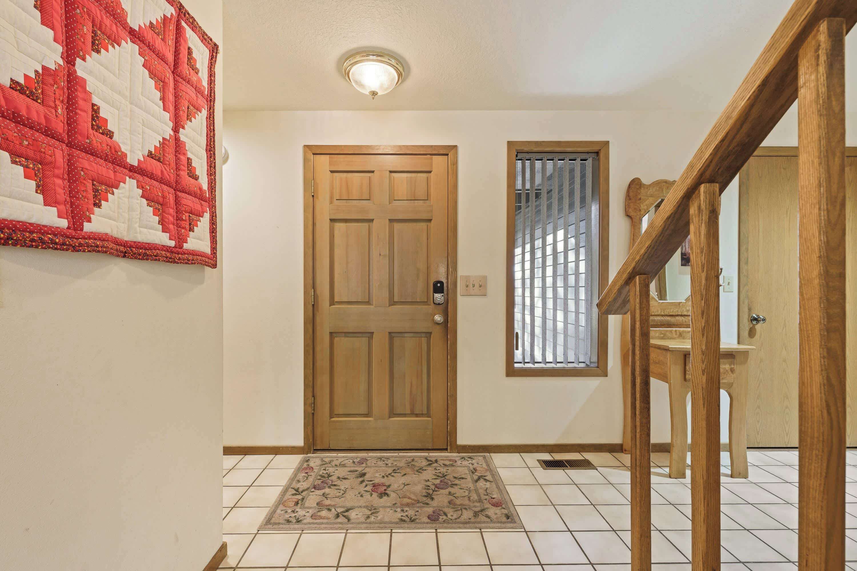 Un couloir avec une porte en bois, une petite fenêtre grillagée, une chaise en bois et un tapis à motifs floraux.