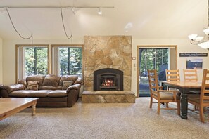 A cozy living room with a stone fireplace, leather sofa, dining table, and chairs. - Blue Goose With Hot Tub & Sharc Access (Bend)